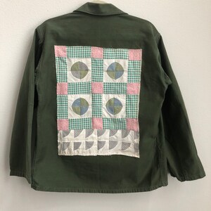 Könnte beinhalten: Eine grüne Utility-Jacke mit einem Patchwork-Steppdesign auf der Rückseite. Die Steppdecke besteht aus Quadraten aus grünem, rosa und weißem Stoff mit einem geometrischen Muster.
