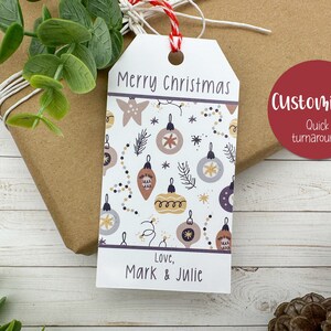 May include: A white Christmas gift tag with a festive ornament pattern and the words "Merry Christmas." The tag is personalized with "Love, Mark & Julie." A red circle with "Customized! Quick turnaround!" is also visible.