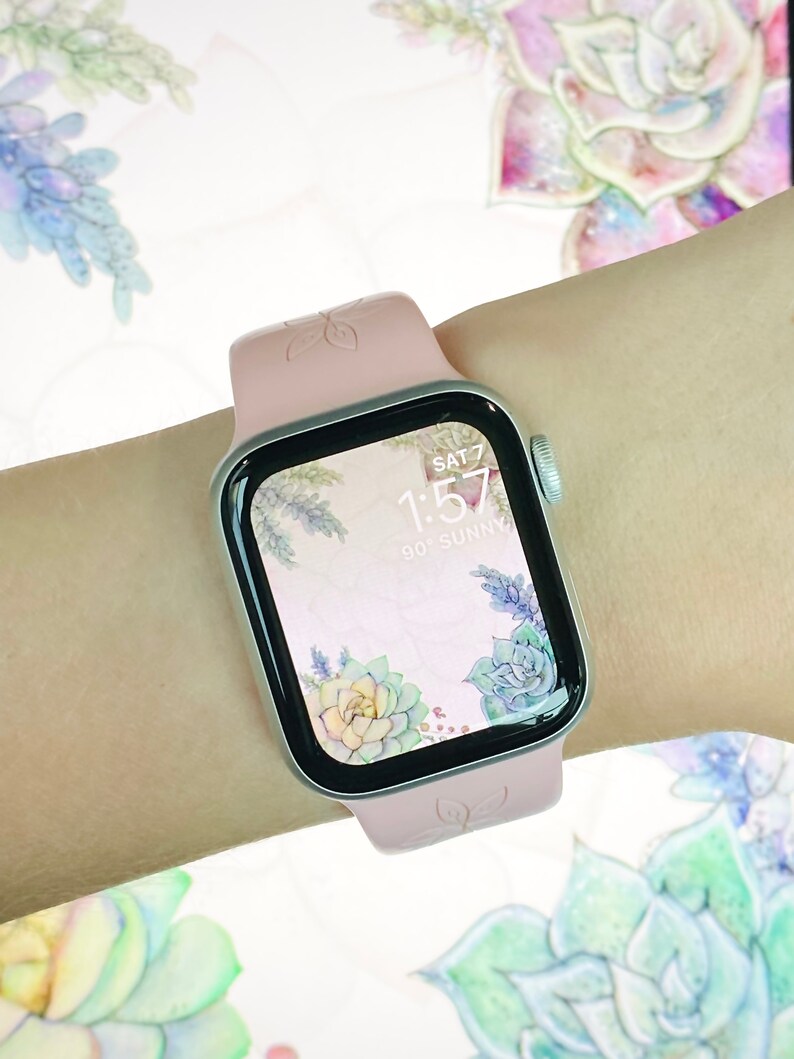 May include: A pink Apple Watch with a floral watch face. The watch face shows the time as 1:57 and the day as SAT 7. The watch face also shows the temperature as 90 degrees and the weather as sunny.