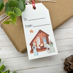 May include: A white gift tag with a nativity scene illustration. The tag has lines for "To:" and "From:" and a gold star above the scene.