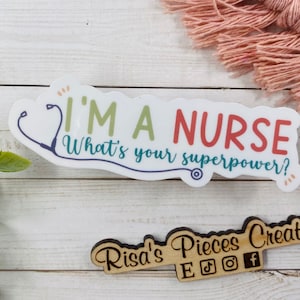 May include: White sticker with a stethoscope graphic and the text "I'm a Nurse What's your superpower?"  The sticker is on a white wooden surface. A wooden sign with the text "Risa's Pieces Creations" and social media icons is in the lower right corner of the image.