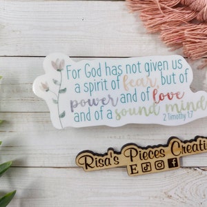 May include: White sticker with a floral design and the text "For God has not given us a spirit of fear, but of power and of love and of a sound mind. 2 Timothy 1:7". A wooden sign with the text "Risa's Pieces Creations" and social media icons.