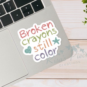 May include: A white sticker with the text "Broken crayons still color" in colorful, hand-drawn lettering. A heart and star are included in the design.