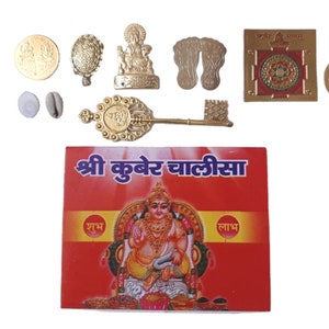 Könnte beinhalten: Eine Sammlung goldfarbener religiöser Gegenstände, darunter eine Münze, eine Schildkrötenfigur, eine Gottheitsstatue, ein Schlüssel und eine rote Karte mit Hindi-Text und einer Illustration einer Gottheit. Die Gegenstände sind auf einer weißen Oberfläche angeordnet.