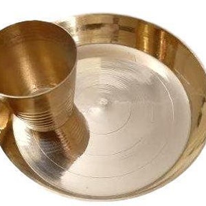 May include: A brass plate with a matching brass cup, both with a shiny finish. The plate has a slightly raised rim and a circular design.