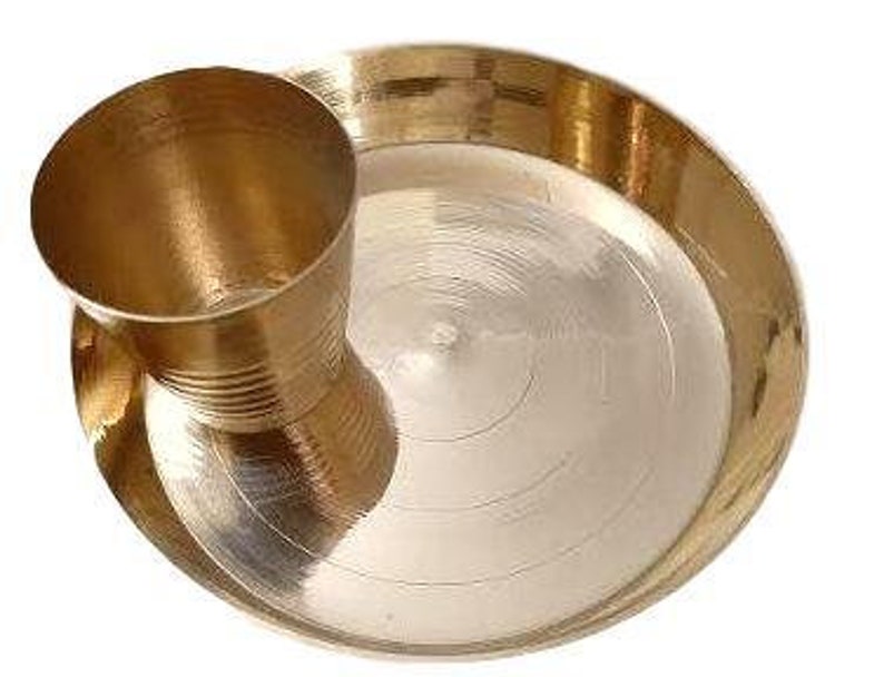 May include: A brass plate with a matching brass cup, both with a shiny finish. The plate has a slightly raised rim and a circular design.