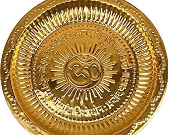 May include: A gold-colored metal plate with a raised design of a sun with rays and the symbol Om in the center. The plate has a decorative border and the words "Shree Ganesha" are inscribed around the sun.
