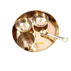 Op de afbeelding: Een messing thali-set met drie kommen en een lepel. De thali is rond en heeft een verhoogde rand. De kommen zijn klein en hebben een gladde, glanzende afwerking. De lepel is lang en dun.