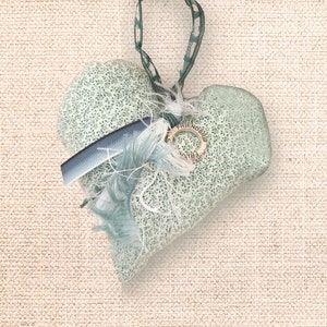 May include: A green ceramic heart ornament with a white and blue fabric embellishment and a metal charm that says "Friendship".
