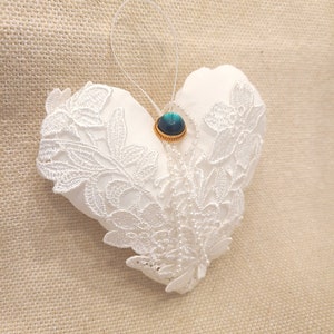 May include: White lace heart-shaped pillow with a teal blue button in the center.
