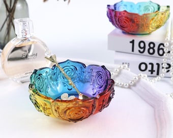 May include: Two rainbow colored glass bowls with a rose design. The bowls are on a white surface with a string of pearls and a book with the text "Year 2005 1986"
