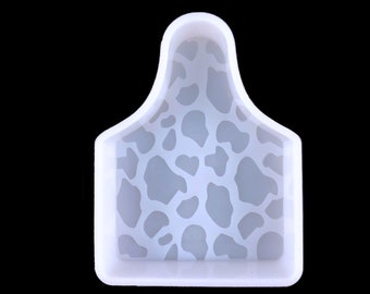 May include: White silicone mould with a cow print design. The mould is shaped like a cow tag.