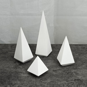 Può includere: Quattro espositori a forma di piramide bianca di diverse dimensioni su una superficie grigia testurizzata.