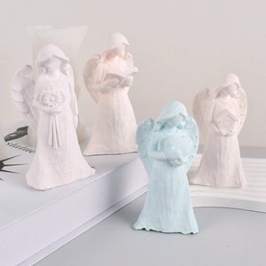 May include: Four small angel figurines, two are white, one is pale pink, and one is light blue. Each angel is holding a different object, including a book, a bird, a bouquet of flowers, and a heart.
