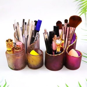 May include: A three-sectioned heart-shaped desktop organizer with a gold glitter trim. The left section holds pens and pencils, the middle section holds makeup brushes and bottles, and the right section holds makeup sponges.