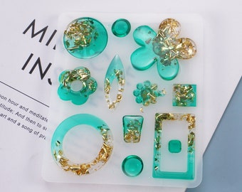 May include: A silicone mold for making resin jewelry. The mold has 10 different shapes, including circles, ovals, squares, and flowers. The mold is filled with clear resin and gold glitter.