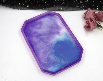 May include: A rectangular resin tray with a purple border and a swirling interior of purple and blue hues. The tray's design resembles a nebula or ocean scene, with a glossy finish. This decorative tray is suitable for serving or display.