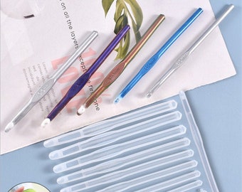 May include: A set of 12 white plastic crochet hooks and four colorful crochet hooks, including a silver, blue, purple, and gold hook. The hooks are arranged on a white surface with text that reads "on all the layers except the first one".