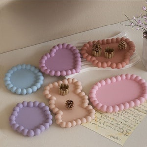 Peut inclure: Cinq plateaux décoratifs avec un motif de perles en relief. Les plateaux sont de différentes couleurs, notamment bleu clair, violet, rose et pêche. Les plateaux sont faits d'un matériau lisse et texturé.