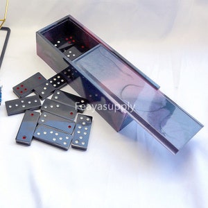 Può includere: Un set di domino neri con punti rossi, in una scatola di marmo nero, rosa e blu. La scatola ha un coperchio scorrevole.