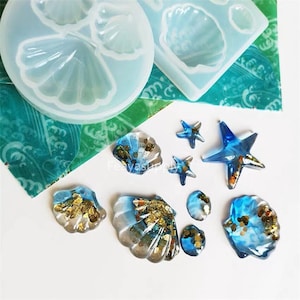 Pode incluir: Um conjunto de moldes de silicone para fazer conchas marinhas e estrelas do mar de resina. Os moldes são mostrados com peças de resina acabadas, incluindo conchas marinhas azuis e douradas e estrelas do mar azuis.