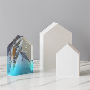 Op de afbeelding: Een transparant harsbeeld van twee walvissen die zwemmen in een blauwe en witte oceaan sc&egrave;ne. Het beeld wordt getoond op een wit marmeren oppervlak met twee witte geometrische vormen erachter.