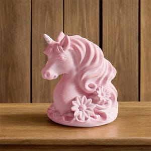 Może przedstawiać: Różowa ceramiczna figurka jednorożca ze spiralnym rogiem, płynącą grzywą i kwiatowymi akcentami. Rzeźba jest prezentowana na drewnianej powierzchni, ukazując jej szczegółowy design i delikatny kolor.