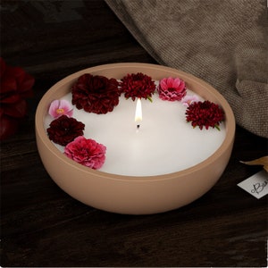 May include: A brown ceramic bowl candle with a white wax top and a lit wick. The candle is decorated with red and pink flowers.