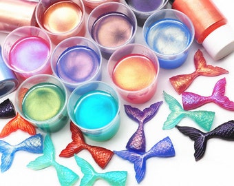 May include: Assortment of iridescent resin in small cups with mermaid tail charms. The resin colors include blue, green, purple, pink, orange, and gold.