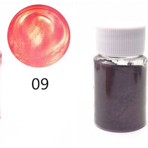 K&ouml;nnte beinhalten: Zwei kleine Flaschen mit metallischem Pigmentpulver. Die Flasche links enth&auml;lt ein goldfarbenes Pulver. Die Flasche rechts enth&auml;lt ein violettes Pulver. Die Flaschen sind mit 09 und 10 beschriftet.