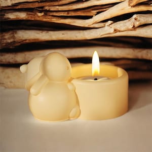 Könnte beinhalten: Ein weißer Kerzenhalter in Form eines kleinen Tieres mit einer brennenden Teelichtkerze im Inneren.