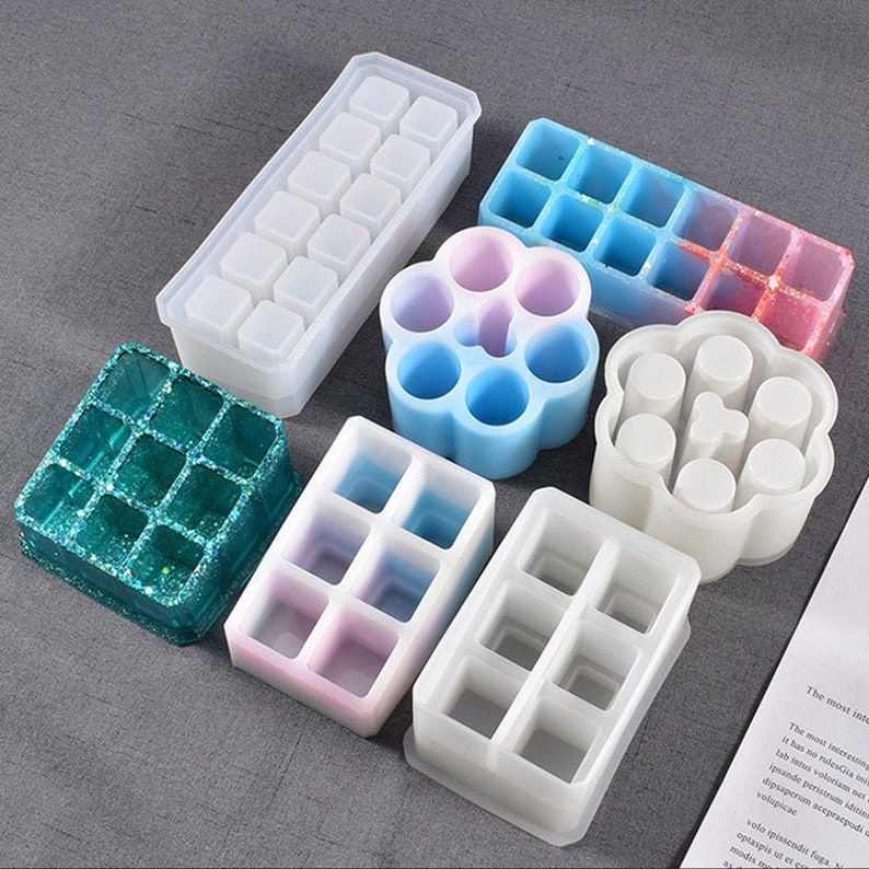 May include: Set of nine silicone molds for crafting. The molds are in various shapes and sizes, including a square, a rectangle, a flower, and a circle. The molds are made of clear silicone and have a smooth finish.