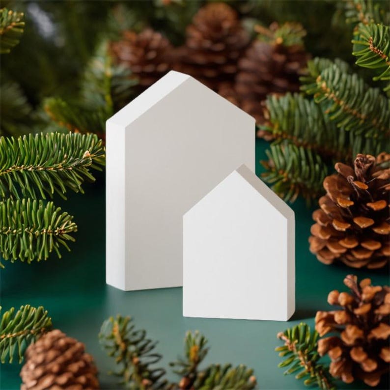 Op de afbeelding: Twee witte houten huisjes, waarvan er &eacute;&eacute;n kleiner is dan de andere, staan op een groene ondergrond. De huisjes zijn omringd door dennentakken en dennenappels.