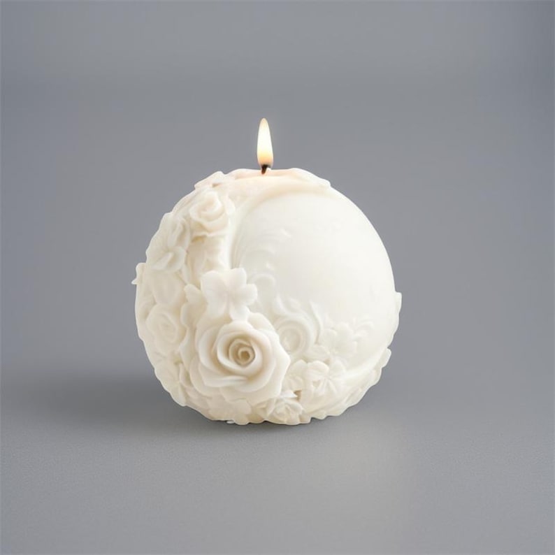 May include: A spherical, ivory-colored candle with a floral design. The candle features a detailed relief of roses and other flowers on one side. A lit wick sits atop the candle, casting a warm glow.