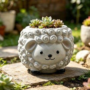 May include: A whimsical, light gray sheep-shaped planter with a smiling face and black accents. The planter is filled with several small succulents. The sheep has curly wool detailing and is sitting on a stone surface.
