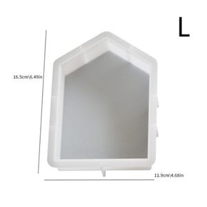 Op de afbeelding: Witte plastic mal voor het maken van betonnen stapstenen. De mal is gevormd als een huis met een puntdak. De mal is 16,5 cm hoog en 11,9 cm breed.