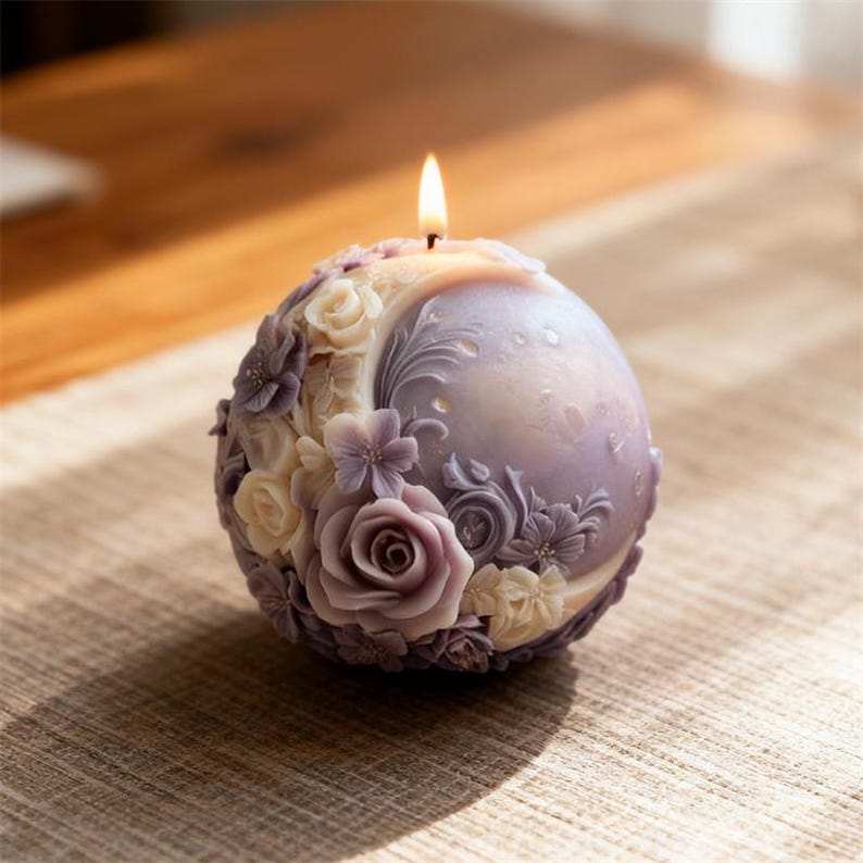 May include: A spherical candle with a lit wick, featuring a detailed floral design. The candle is a soft lavender color, adorned with sculpted roses and other flowers in shades of purple and cream. The candle is approximately 4 inches in diameter.