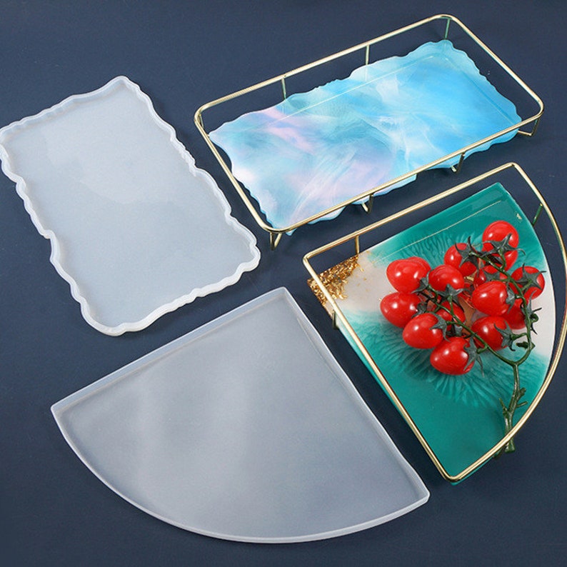 Puede incluir: Tres moldes de silicona transparentes para fundici&oacute;n de resina. Los moldes tienen forma de rect&aacute;ngulo, semic&iacute;rculo y pieza de esquina. Los moldes est&aacute;n sobre una superficie azul oscuro.