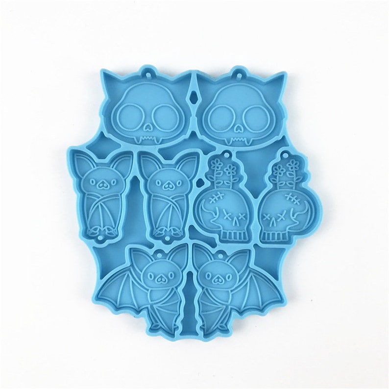 Puede incluir: Molde de silicona azul con ocho formas diferentes de tem&aacute;tica de Halloween: dos murci&eacute;lagos, dos calaveras con flores, dos calaveras con puntadas y dos murci&eacute;lagos con las alas extendidas.
