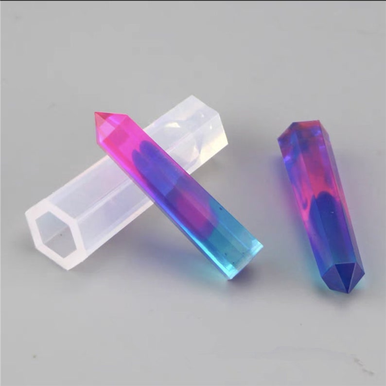 May include: Two clear, hexagonal silicone molds for making resin crystal wands. The molds are shown with two finished resin wands, one with pink and blue swirls and the other with a blue and purple swirl.