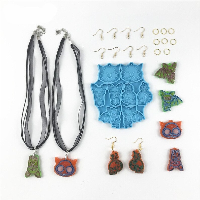 Puede incluir: Un conjunto de suministros para hacer joyas con tem&aacute;tica de Halloween. El conjunto incluye un molde de silicona azul con varios dise&ntilde;os de murci&eacute;lagos y calaveras, cinta negra, anillos de salto dorados, ganchos para pendientes dorados y piezas de resina acabadas de murci&eacute;lagos, calaveras y una botella de poci&oacute;n.