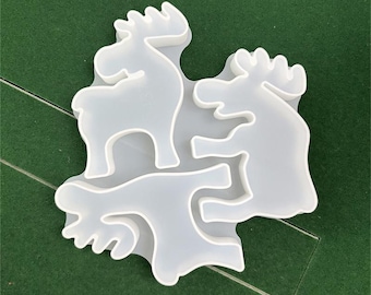 May include: A clear, silicone mold featuring three moose shapes. The mold is designed for crafting and creating decorative elements. The moose shapes are detailed with antlers and a standing pose. The mold is on a green surface.