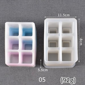 May include: Two silicone molds for making resin crafts. The mold on the left has six compartments and is 5.5 inches tall and 3.75 inches wide. The mold on the right has six compartments and is 8 cm tall and 11.5 cm wide. Both molds are white and have a smooth surface. The text "05 (92g)" is printed below the molds.