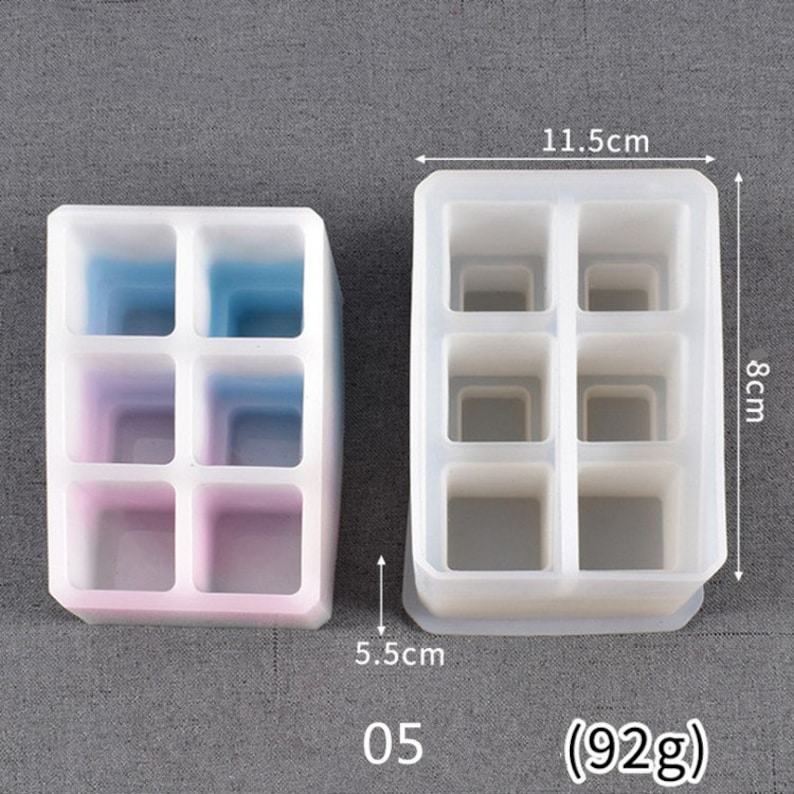 May include: Two silicone molds for making resin crafts. The mold on the left has six compartments and is 5.5 inches tall and 3.75 inches wide. The mold on the right has six compartments and is 8 cm tall and 11.5 cm wide. Both molds are white and have a smooth surface. The text "05 (92g)" is printed below the molds.