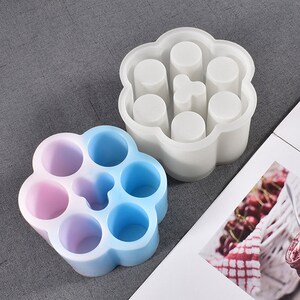 May include: Two silicone molds for making candles or soap. The molds are shaped like a flower with six round cavities. One mold is white and the other is blue and pink.