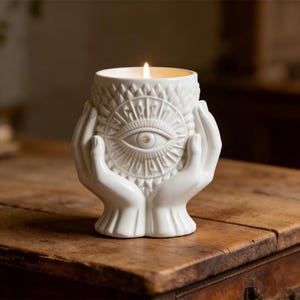 Puede incluir: Una taza de cerámica blanca con un asa negra y el texto "But First, Coffee" en negrita negra. La taza se encuentra sobre un fondo borroso, sugiriendo un ambiente acogedor.
