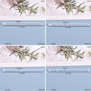 May include: Four clear plastic tubes of different lengths, each measured in centimeters. The tubes are laid out on a white surface with a green plant in the background.