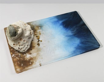 May include: A rectangular tray with a blue and white ocean-inspired design. The tray has a brown sand-like texture at the bottom and a white seashell on top.