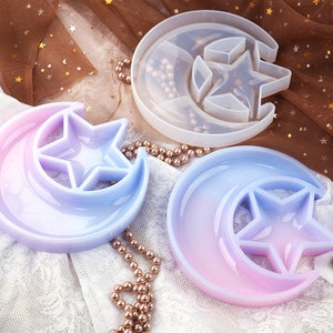 May include: Three silicone molds for resin casting in the shape of a crescent moon with a star inside. The molds are in different colors: white, light blue, and pink.