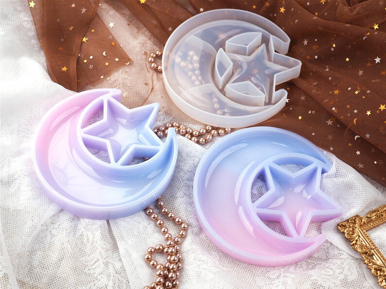 May include: Three silicone molds for resin casting in the shape of a crescent moon with a star inside. The molds are in different colors: white, light blue, and pink.